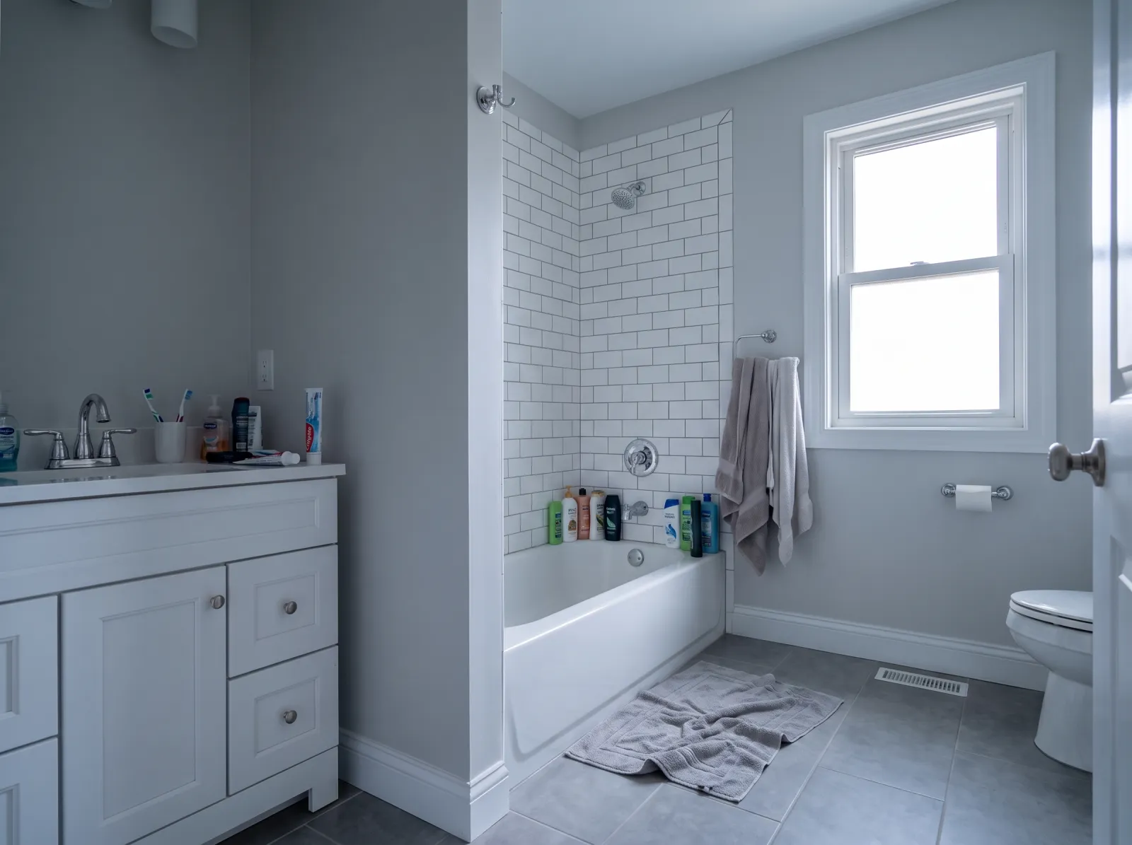 Main bathroom straight off the phone: cold grey cast, bottles, crooked towels